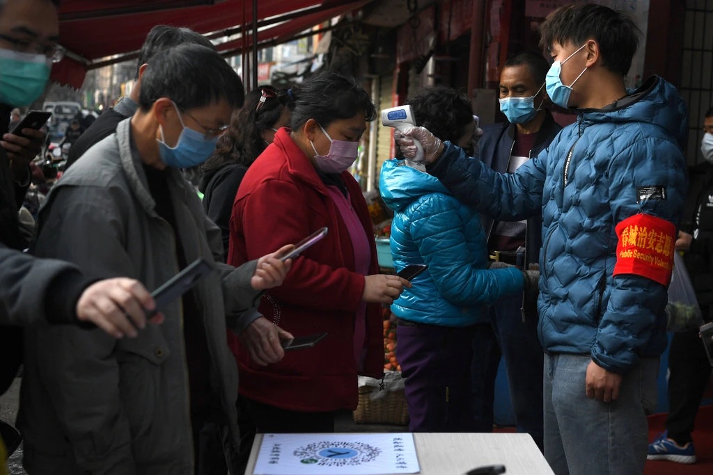 People scanning a QR code on their phones while volunteers check their temperatures before entering a market