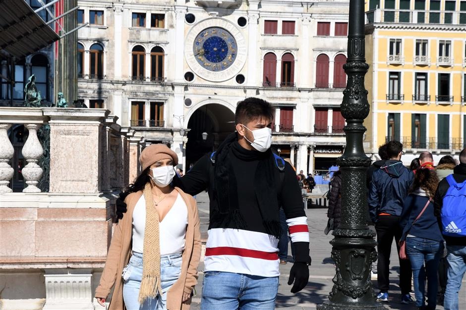Tourists wearing a protective face mask walk on San Marco square in Venice