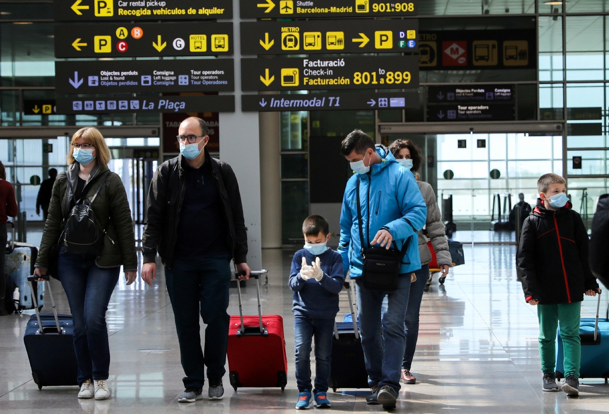 Families wear protective face masks as they walk with their luggage at Tarradellas Barcelona El Prat Airport