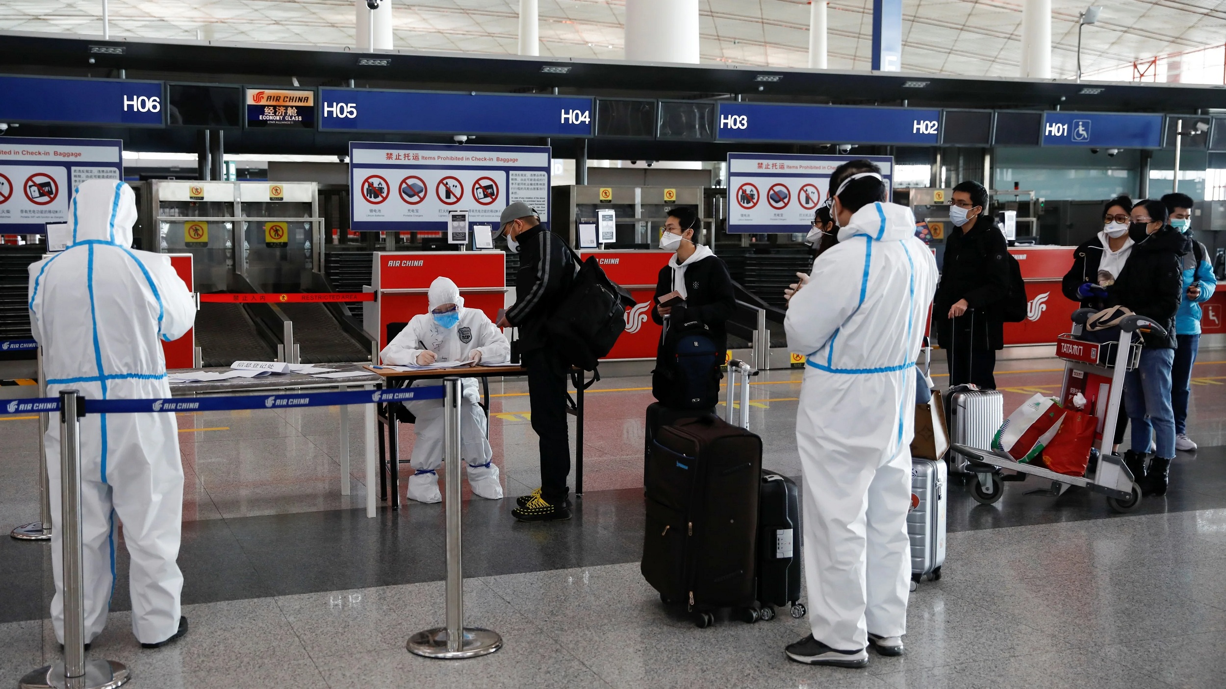 Staff members wearing protective suits register passengers in front of a check in counter of Air China at Beijing Capital International Airport