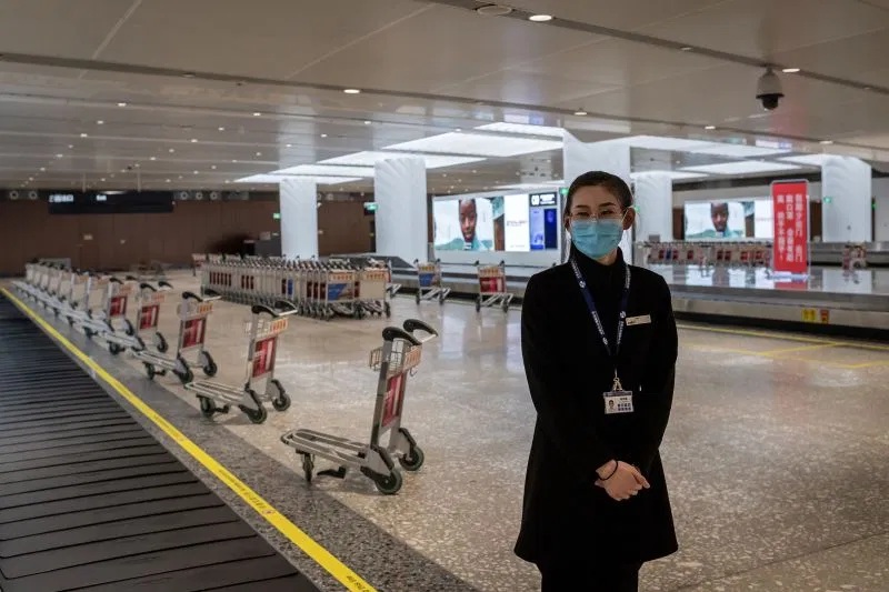 an airport worker wearing a face mask while standing next to an empty baggage claim area at Daxing international airport in Beijing