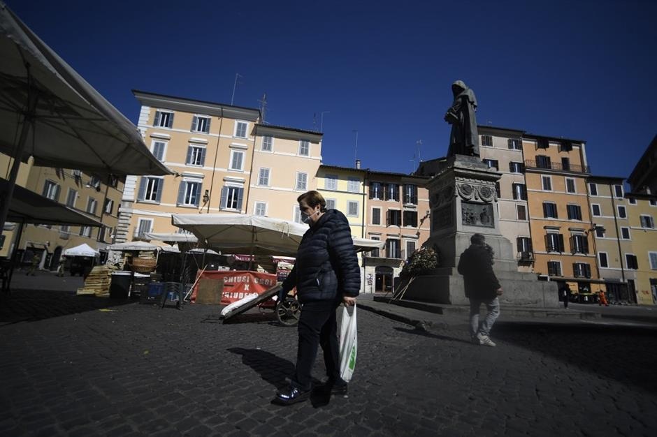 A woman wearing a face mask walks across the Campo dei Fiori market square on March 16