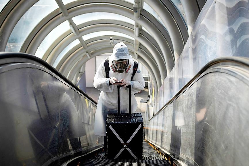 A traveler wearing protective clothing and a full face mask rides an escalator after leaving Beijing Railway Station