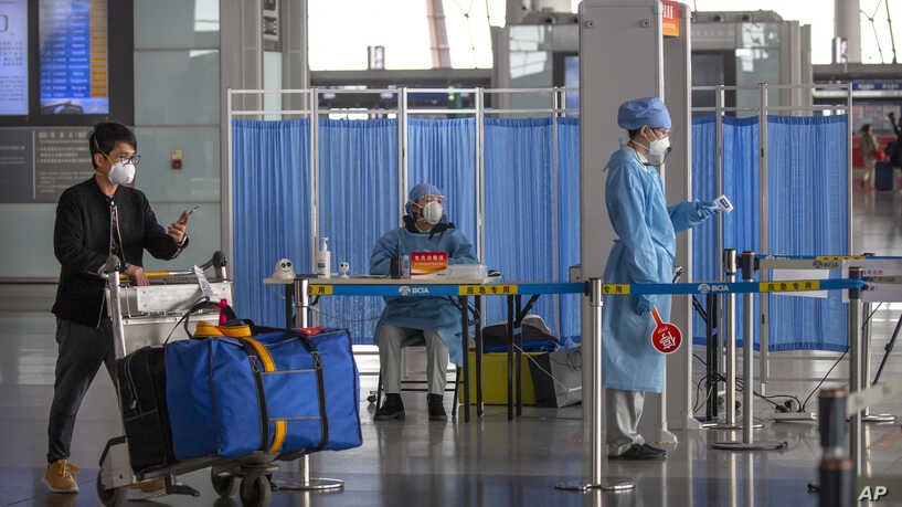 A man pushes his luggage past workers in protective suits as they wait to take the temperature of travelers at Beijing Capital International Airport in Beijing March 6