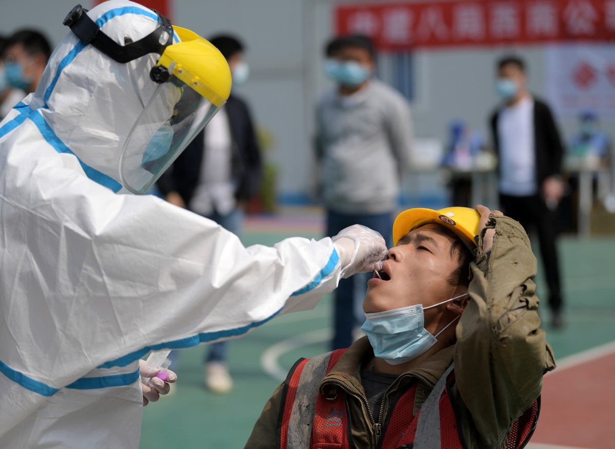 A worker in a protective suit collects a swab from a construction worker for nucleic acid test in Wuhan Hubei province