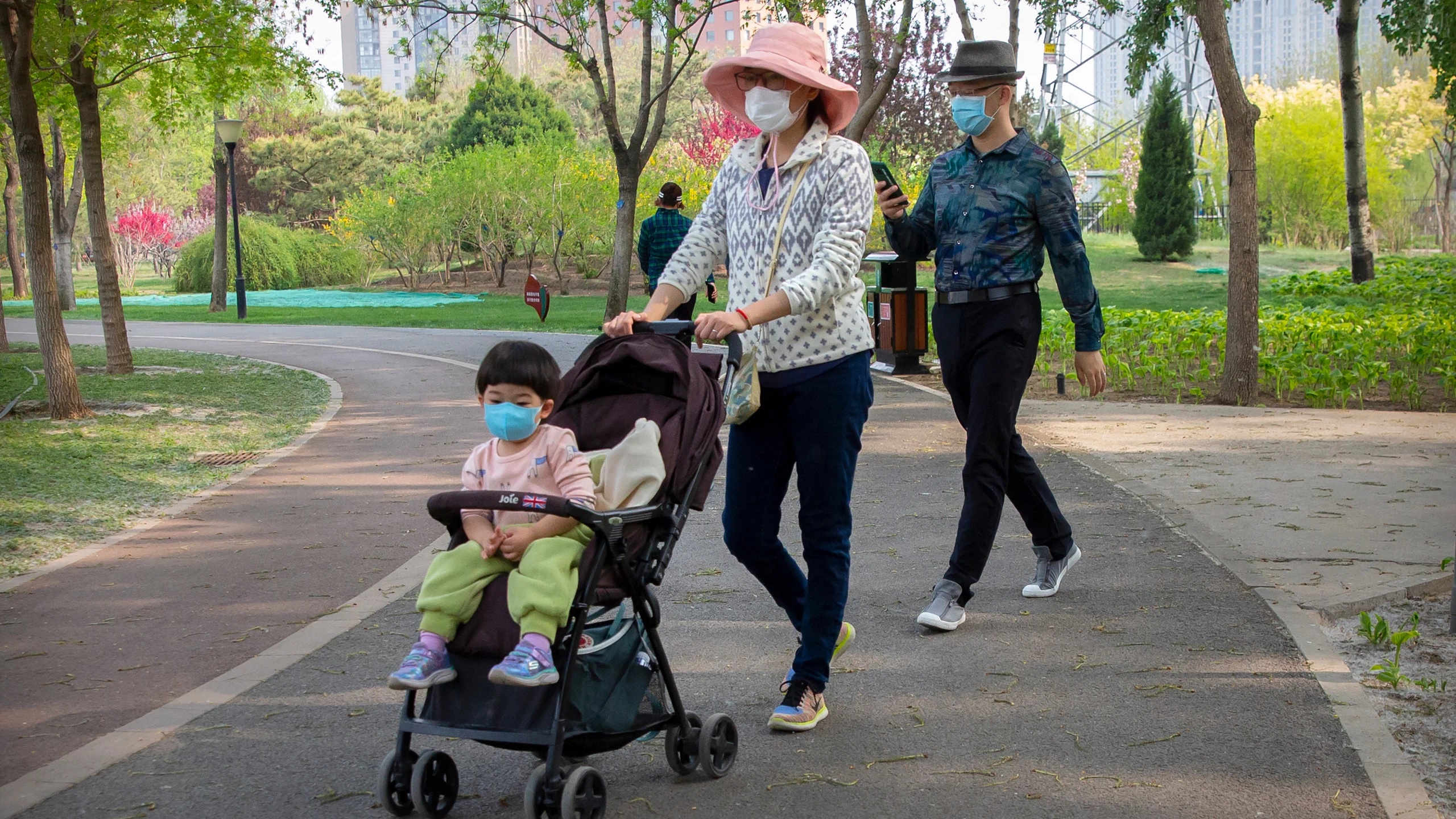 People face masks to protect against the spread of the new coronavirus as they walk through a public park in Beijing