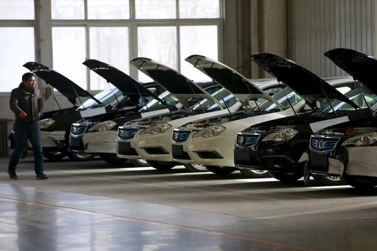 A man walks past cars at an assembly line producing electronic cars at a factory of Beijing Electric Vehicle