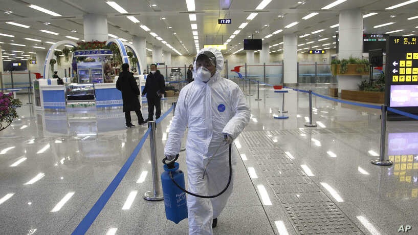 A staff member in protective gear carries a disinfectant spray can