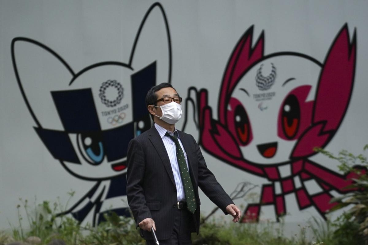 A man with a face mask against the spread of the new coronavirus walks in front of Miraitowa and Someity mascots for the Tokyo 2020 Olympics and Paralympics at a park in Tokyo