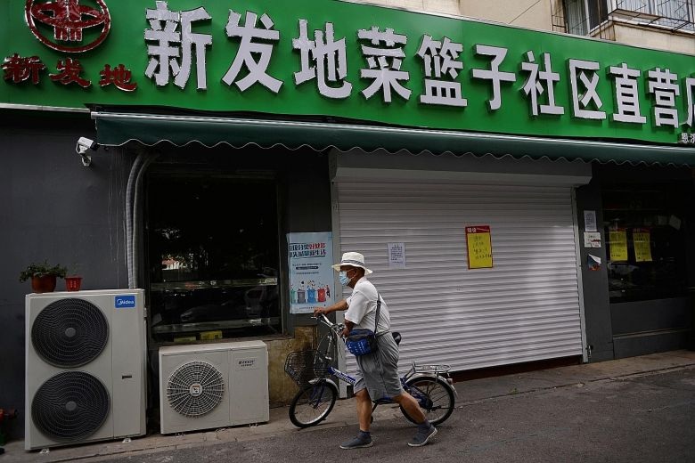 A man wheeling his bicycle past a one day closure sign at the entrance of a convenience store that sells produce from the Xinfadi wholesale market in Beijing