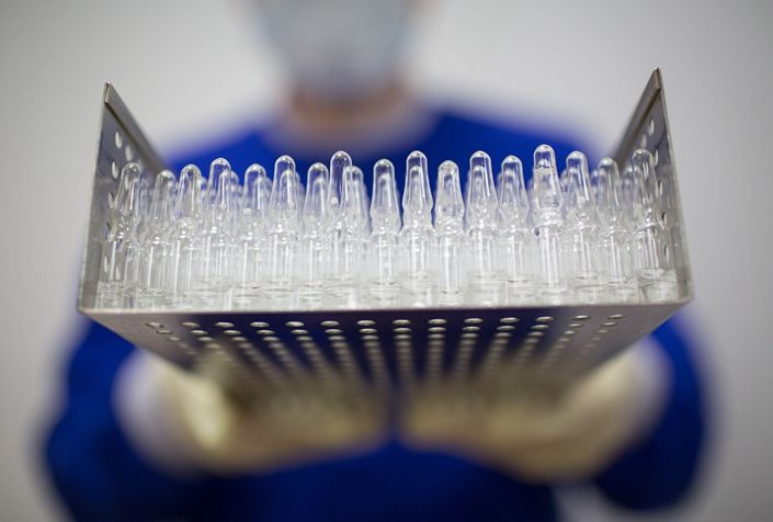 A worker wearing personal protective equipment holds a tray containing unlabeled ampoules of the Covid 19 vaccine