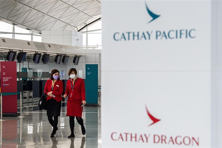 Employees walk past signage for Cathay Pacific and Cathay Dragon near the citys flagship carrier check in counters at Hong Kong International Airport
