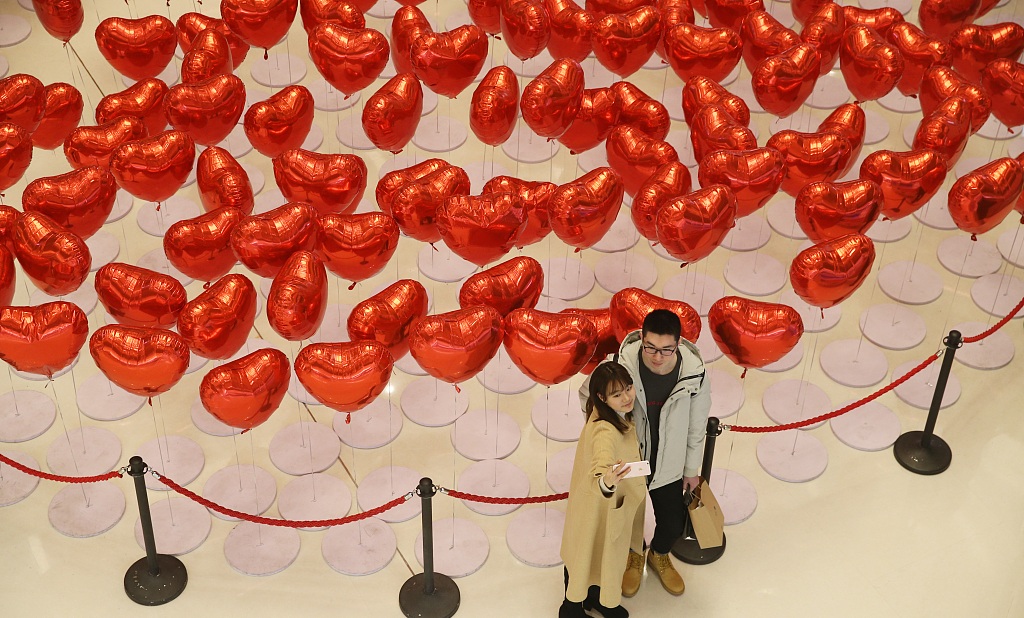 Two lovers take a photo in a shopping mall decorated with heart shaped balloons in Qingdao East Chinas Shandong province