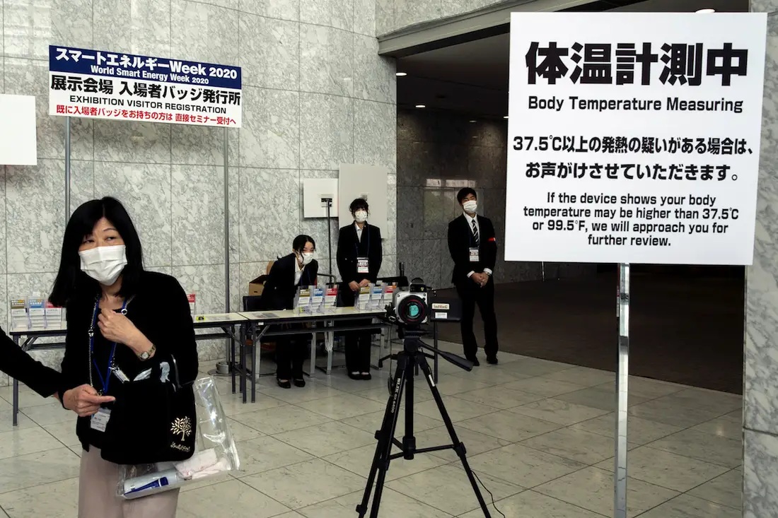 People near a machine measuring body temperature at a convention hall in Tokyo