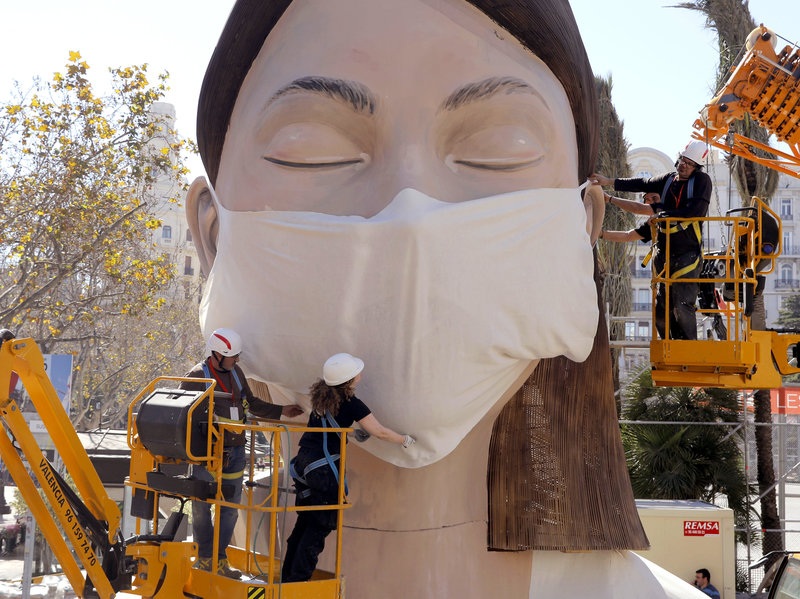 workers in Spain place a medical mask on a figure that was to be part of the Fallas festival in Valencia