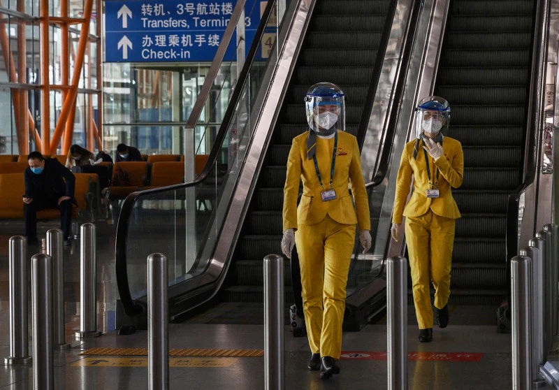 Chinese tourist information clerks wear protective masks and visors in the arrivals area at Beijing Capital International Airport on March 24