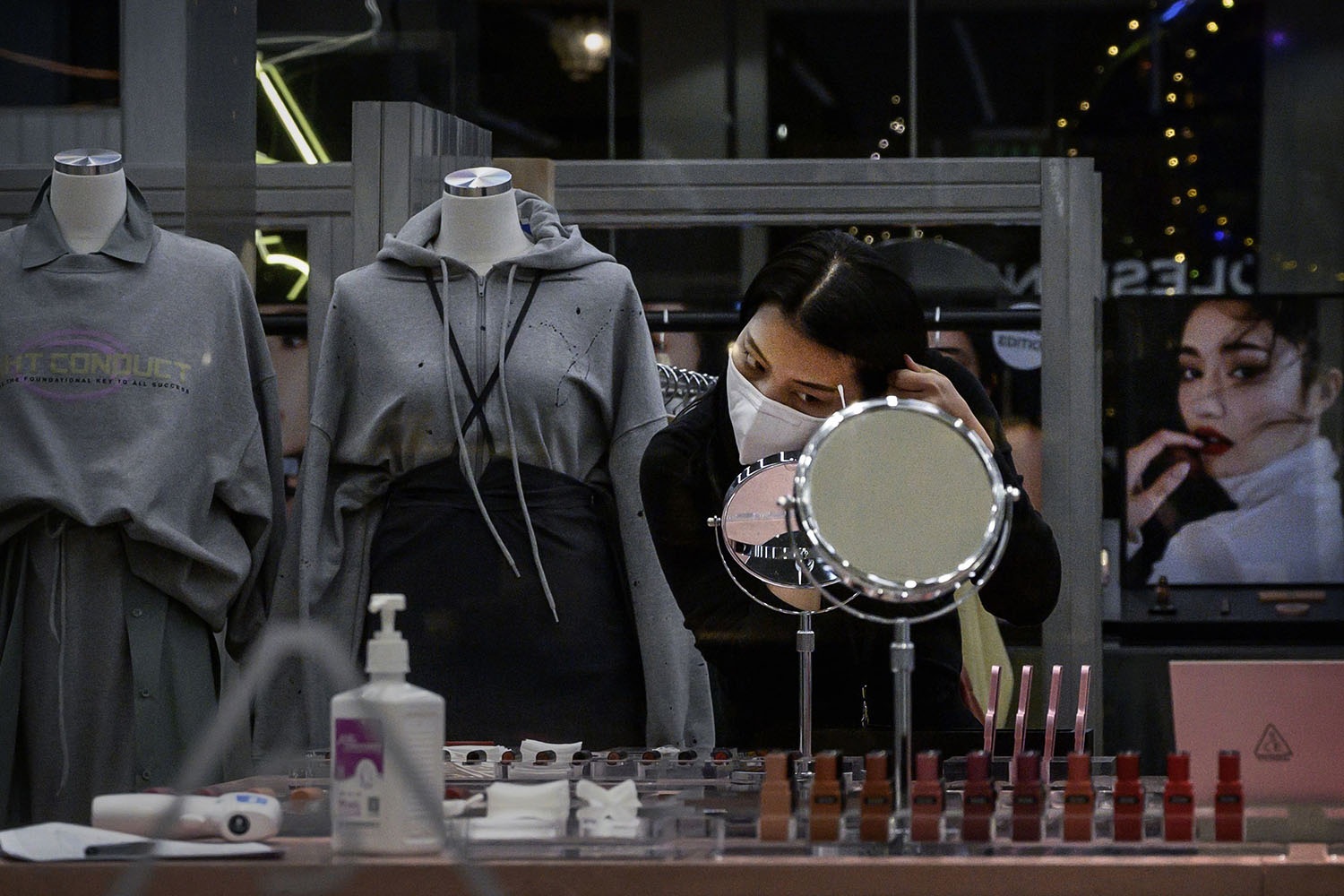 A Chinese woman wears a protective mask as she puts on makeup while waiting for customers at a clothing store in Beijing